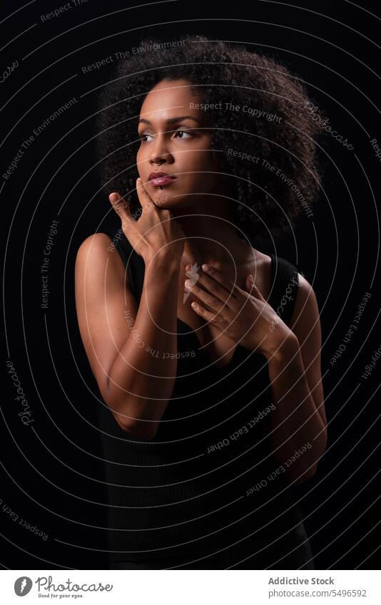 Pensive ethnic woman touching face in dark studio serious portrait model individuality millennial pensive stare curly hair calm confident appearance young afro