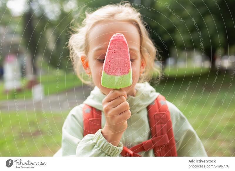 Girl with backpack standing near grassy field and enjoying ice cream child park path cute childhood green kid girl adorable summer sweet carefree wavy hair