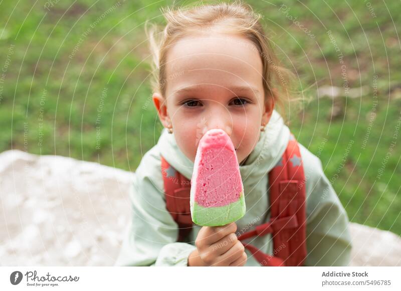 Happy kid with backpack standing near grassy field and enjoying ice cream child park smile path happy cheerful cute childhood green girl adorable summer sweet