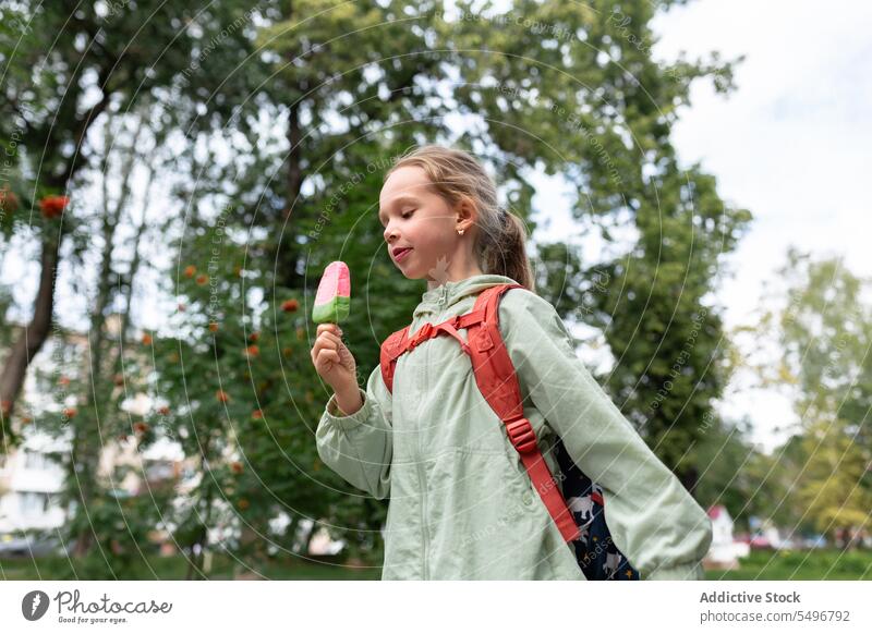 Happy kid with backpack standing in green park and enjoying ice cream in daylight child childhood grass happy eat cute adorable girl field carefree tasty