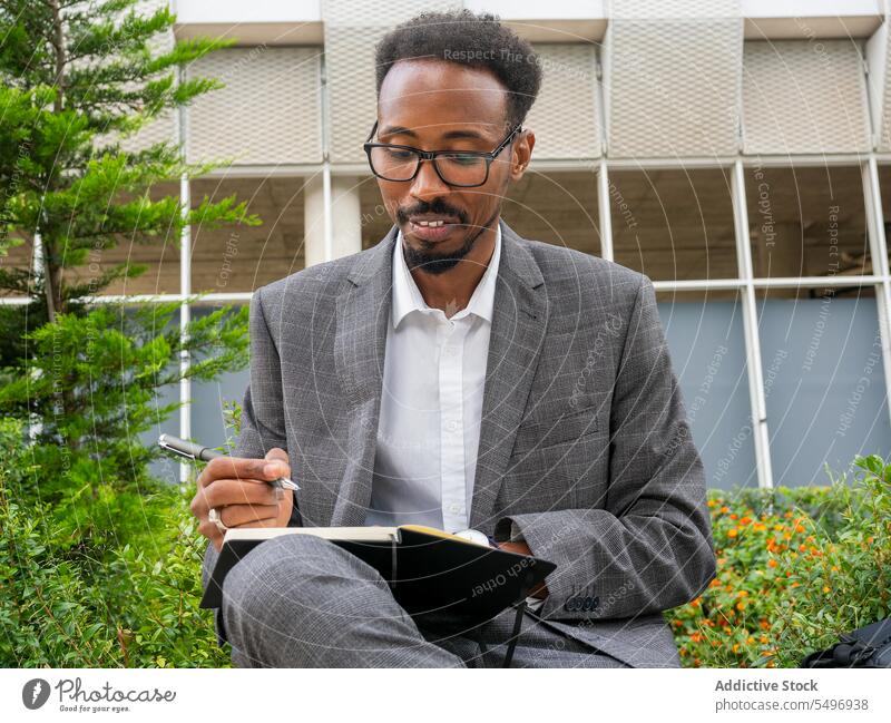 Black man writing in notebook on city street take note write businessman planner male african american focus urban black suit eyeglasses formal pen well dressed
