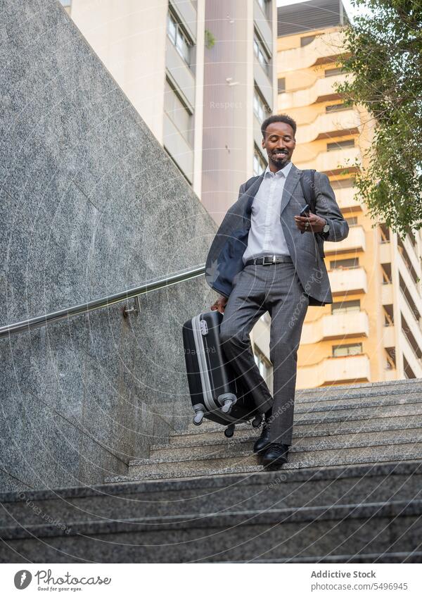 Cheerful black man with suitcase walking downstairs while browsing on smartphone underground phone call happy formal staircase stairway businessman male device