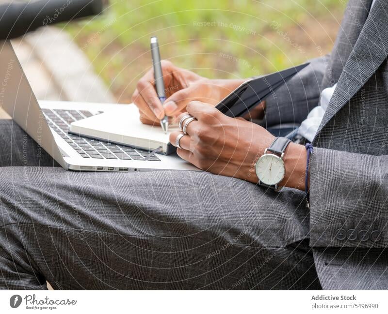 Unrecognizable businessman writing in notepad with pen while sitting with laptop in daylight take note entrepreneur write notebook suit park summer male formal