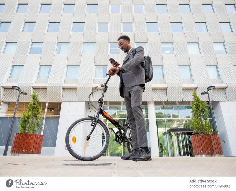Black businessman with smartphone and bicycle chat focus formal city street phone call browsing suit male african american black bike text urban device gadget