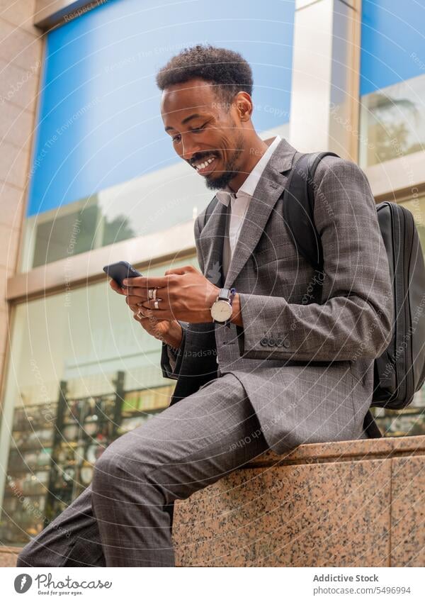 Happy black good looking male using mobile phone on street businessman entrepreneur smartphone browsing employee texting formal elegant executive ethnic