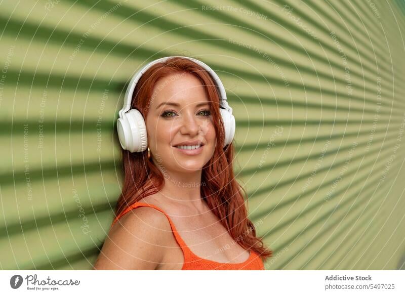 Happy woman listening to music against green wall headphones happy smile cheerful using leisure carefree casual female young joy lifestyle modern device song