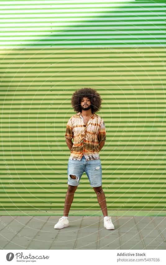 Young ethnic man on sidewalk near wall style street serious urban green stripe trendy male casual young african american curly hair city modern black calm