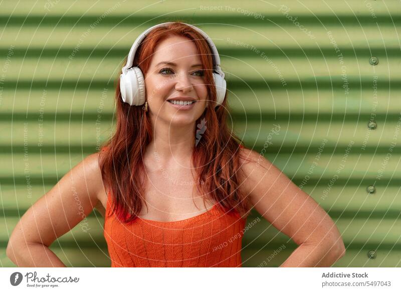 Happy woman listening to music against green wall headphones happy smile cheerful using dance leisure carefree casual female young joy lifestyle modern device