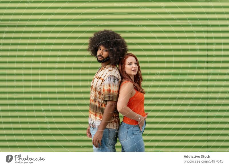 Multiracial couple standing back to back on green background soulmate relationship fondness bonding girlfriend portrait model studio afro curly hair hairstyle