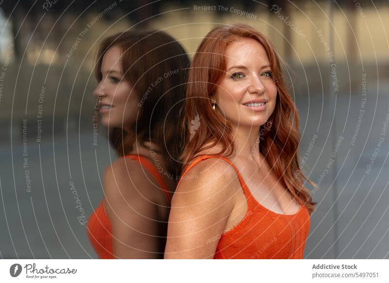 Smiling redhead woman standing against glass wall portrait reflect reflection appearance individuality lean on building street smile toothy smile content