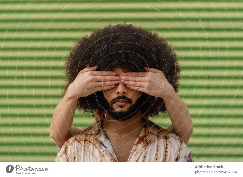 Anonymous friend covering eyes of curly man in studio guess who cover eyes hide surprise look appearance unexpected curly hair portrait afro hairstyle model