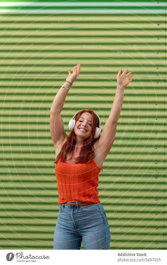 Excited woman dancing to music against wall listen headphones happy arms raised dance smile fun leisure casual female joy song young modern cheerful stripe