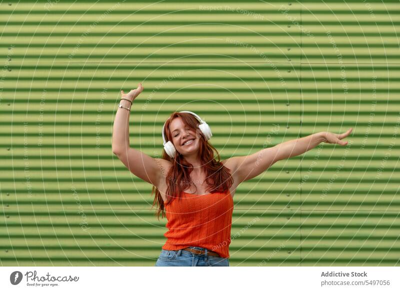 Excited woman dancing to music against wall listen headphones happy arm raised dance smile fun leisure casual female joy song young modern cheerful stripe