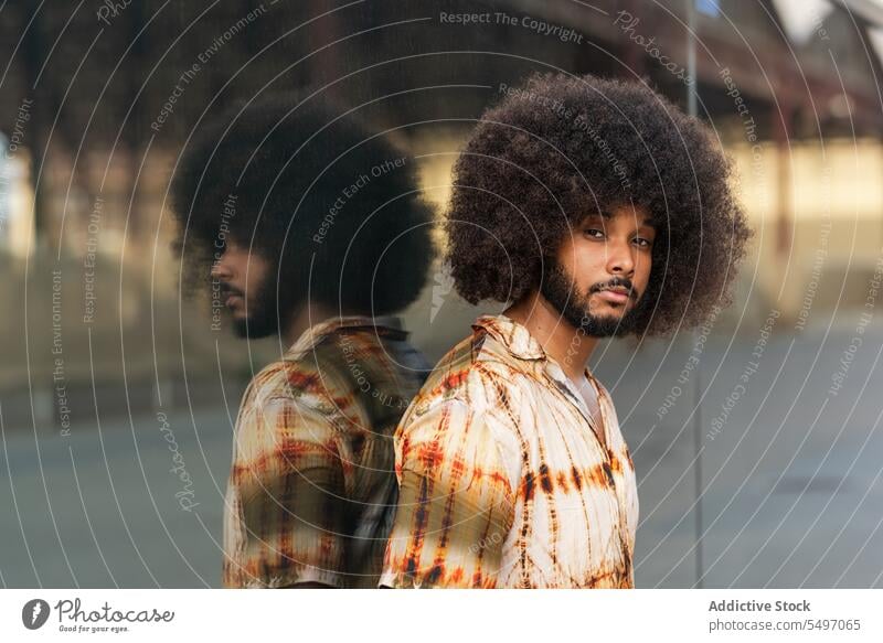 Guy with Afro hairstyle looking at camera against mirrored wall man street appearance curly hair reflection afro portrait male beard shirt ethnic guy hispanic
