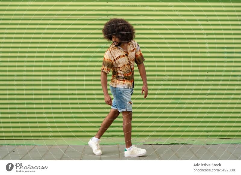 Young ethnic man walking on sidewalk near wall style street serious urban green stripe trendy male casual young african american curly hair city modern black