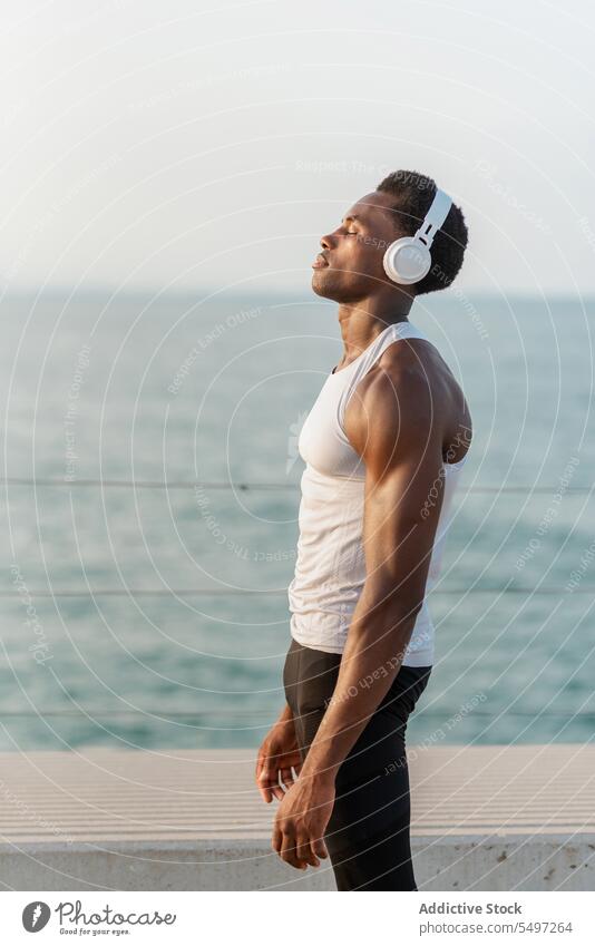 Thoughtful black man with headphones near sea music listen pensive song wireless sound device male water melody calm tranquil dreamy african american