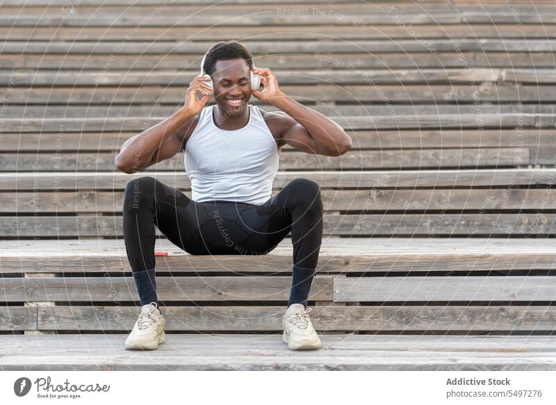 Black sportsman in headphones enjoying music on stairs athlete listen song sportswear relax slim male black african american model fit muscular slender strong