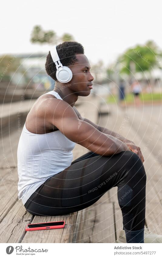 Delighted black sportsman in headphones enjoying music athlete listen song smartphone staircase portrait male african american model fit muscular strong slim