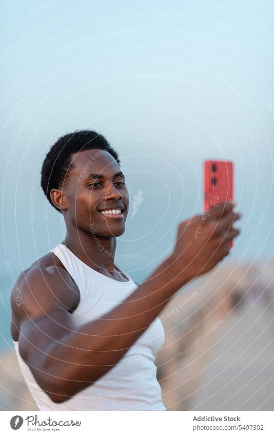 Cheerful black man taking selfie on smartphone happy embankment sea positive smile glad device male mobile gadget cheerful memory take photo enjoy optimist