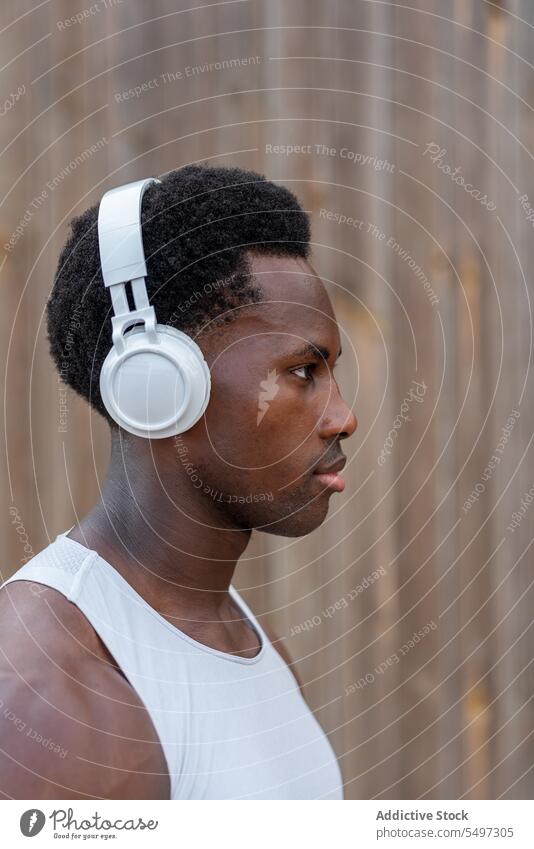 Fit young African American sportsman with headphones near wooden wall listen music workout athlete put on confident portrait power muscular song wireless male