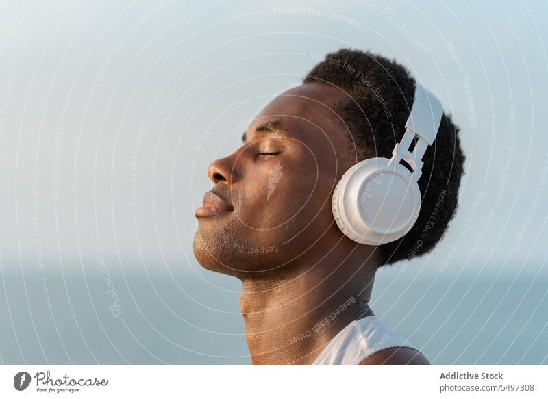 Thoughtful black man with headphones near sea music listen pensive song wireless portrait sound device male water melody calm tranquil dreamy african american