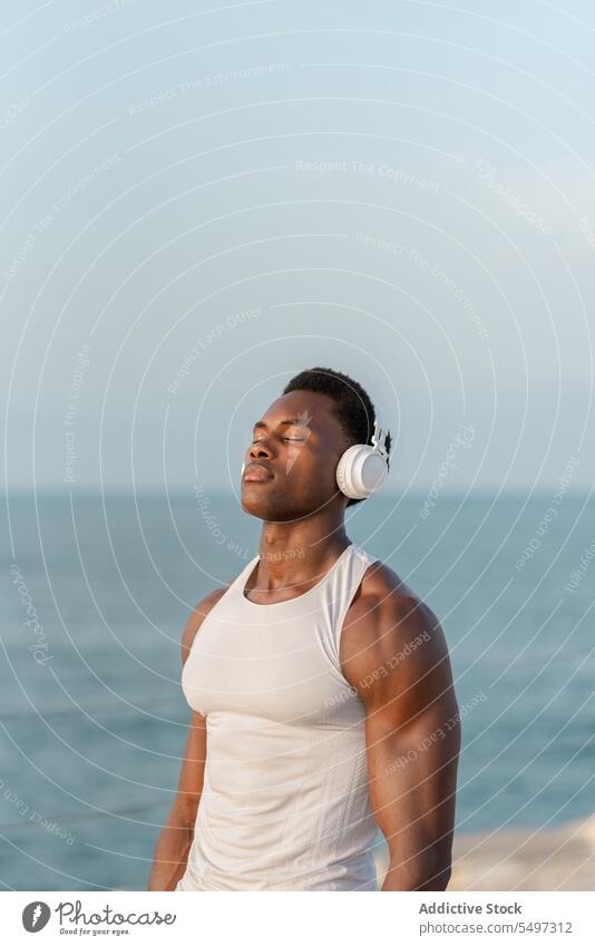 Thoughtful black man with headphones near sea music listen pensive song wireless sound device male water melody calm tranquil dreamy african american