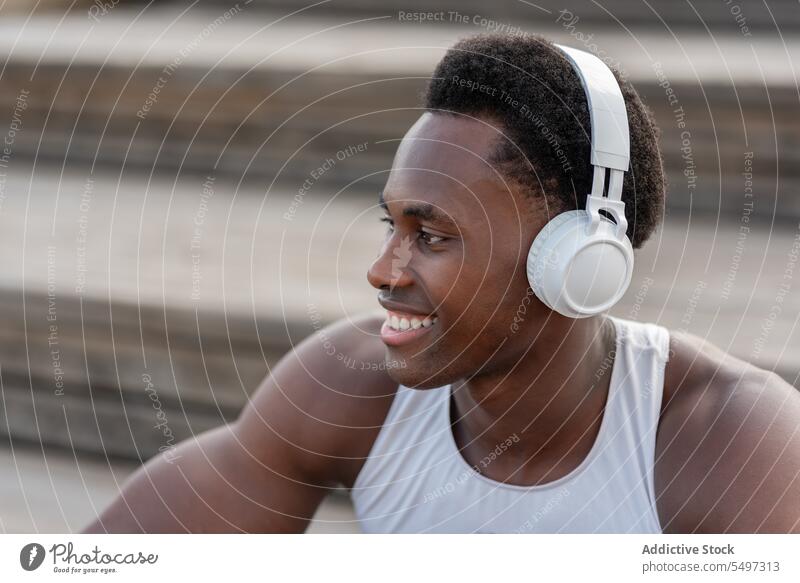 Delighted black sportsman in headphones enjoying music athlete listen song staircase portrait male african american model fit muscular strong slim sportswear