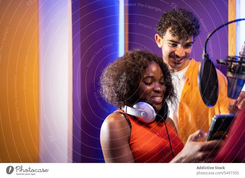 Man and black woman listening to recorded song on smartphone vocalist write music studio result happy african american professional singer star musician perform