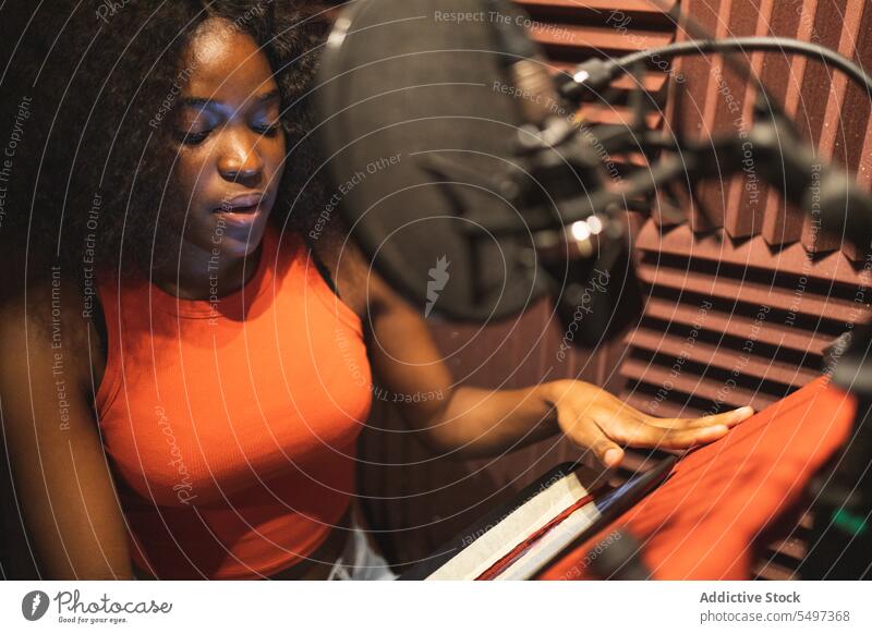 Focused black female standing and recording song near microphone equipment in studio woman singer paper focus audio young african american ethnic read sound