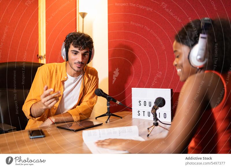 Ethnic colleagues in headphones smiling during online recording podcast man woman microphone tablet communicate smile remote male female young hispanic