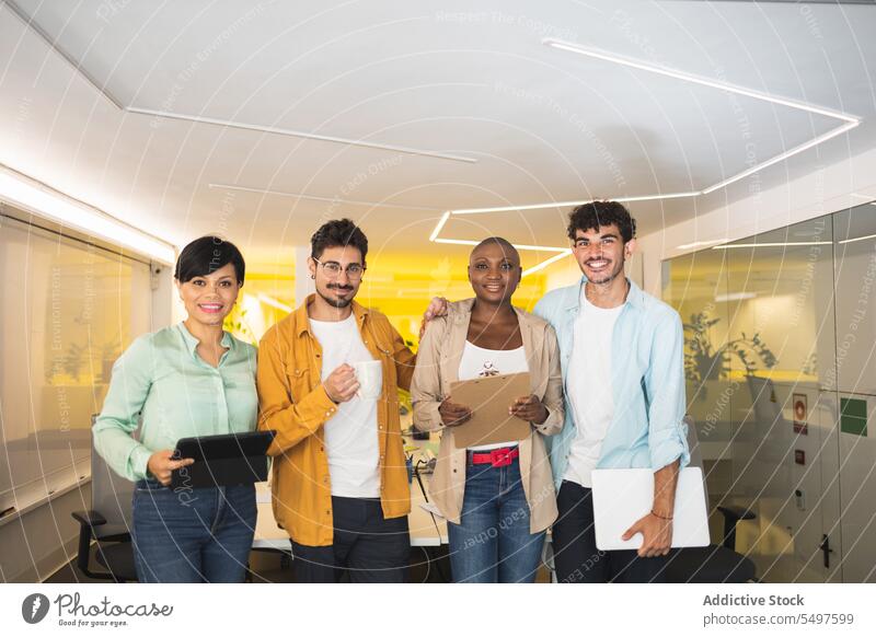 Happy multiethnic coworkers standing together in office colleague laptop workspace workplace tablet smile folder coffee group diverse multiracial cheerful team