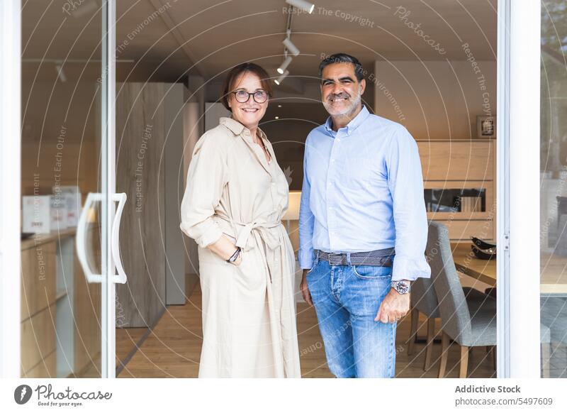 Happy ethnic couple standing in furniture store at entrance in daylight smile owner man happy positive confident shop male female adult husband wife eyeglasses