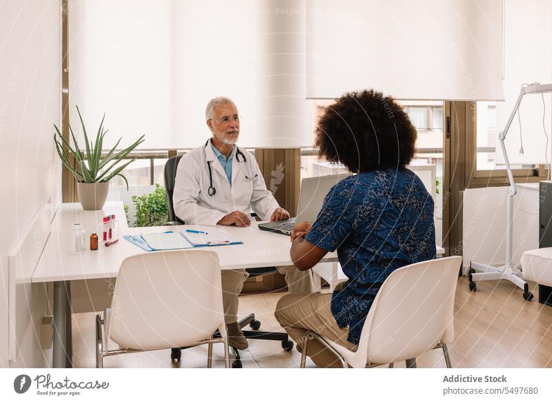 Mature man diagnosing anonymous black patient at appointment practitioner medic clinic check up consult diagnose laptop male african american doctor physician