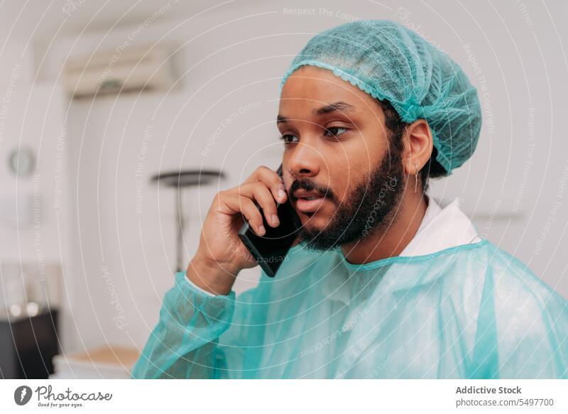 Ethnic male medic having phone call in clinic man smartphone talk surgeon serious doctor hospital concentrate work surgery specialist mixed race ethnic beard