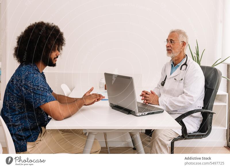 Mature man diagnosing black patient at appointment practitioner medic clinic check up consult diagnose laptop male african american doctor physician examine