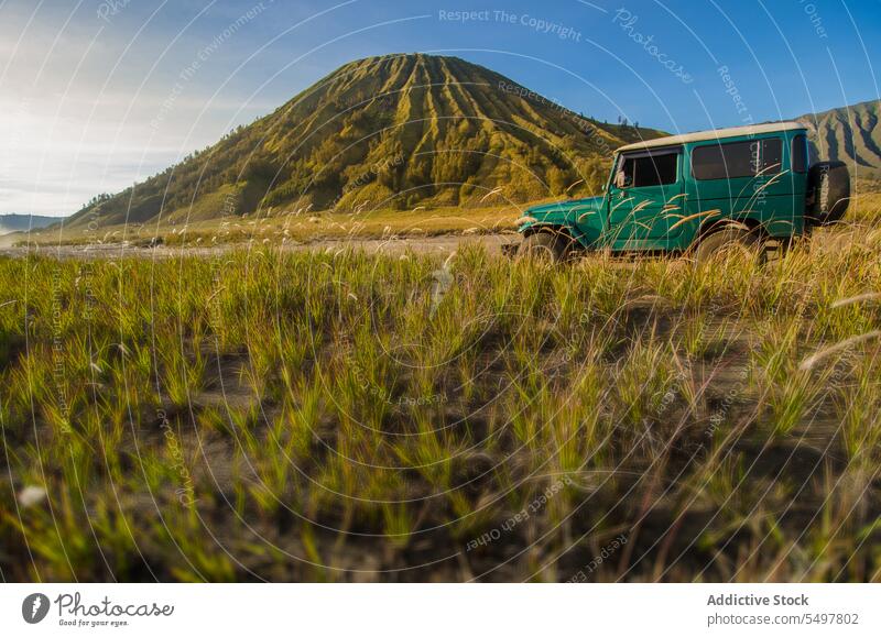 Scenic view of volcano on green land with parked car in daylight amazing scenery mountain range highland environment ridge blue sky landscape formation geology