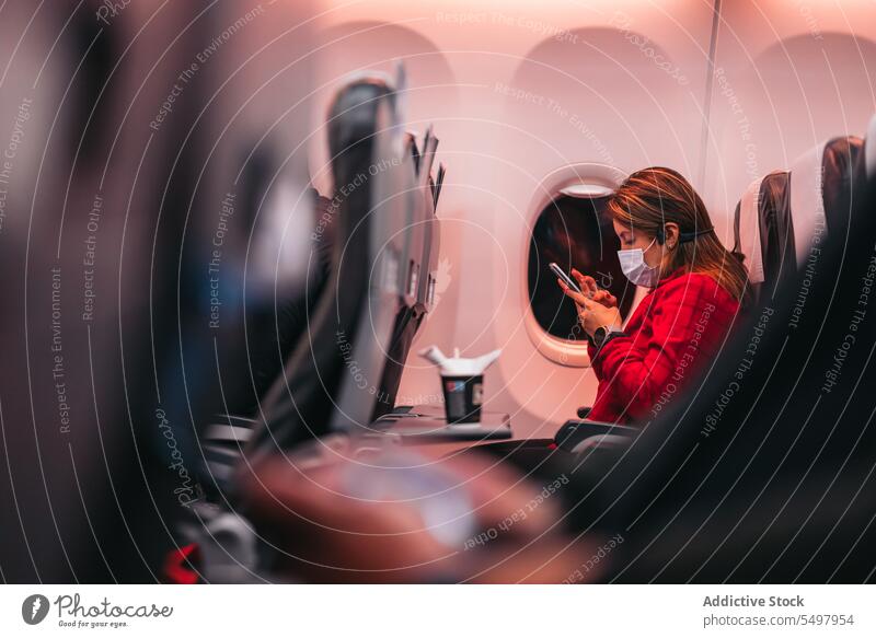 Woman wearing mask while using smartphone in airplane woman passenger coronavirus seat safety protect night new normal flight covid 19 female mobile pandemic