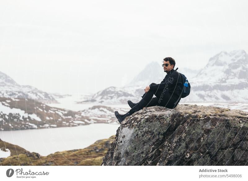 Man sitting on rocky edge and enjoying mountainous landscape man traveler nature highland winter admire terrain male journey range snow wanderlust adventure