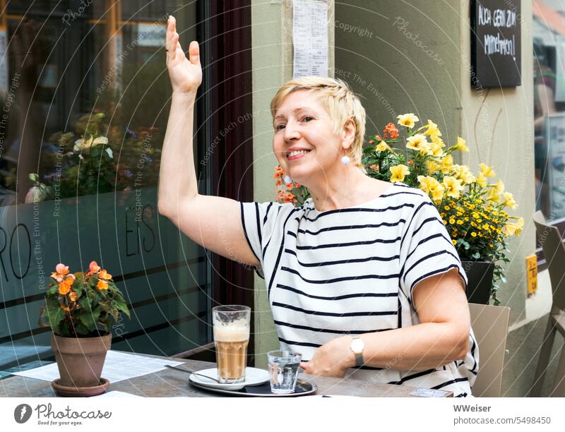 A fashionable woman in her prime sits in a cafe and cheerfully waves to a friend with whom she has a date Woman Chic Attractive kind Mature Wave Sign attention