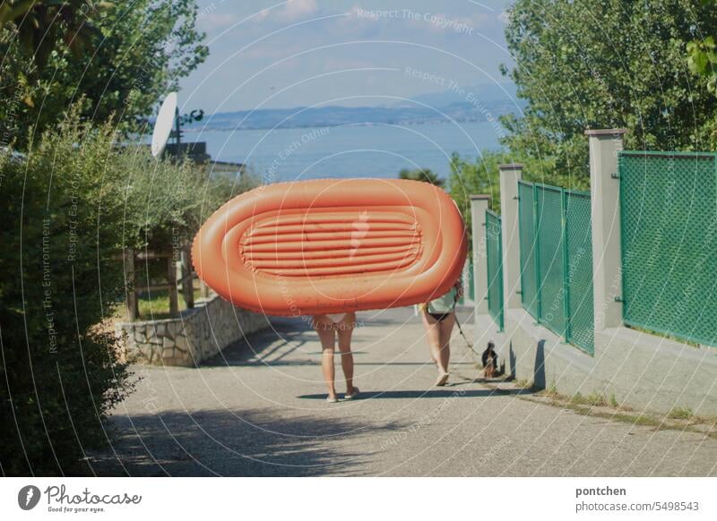 two women in bikini carry orange inflatable boat in Dinghy Bikini Carrying Lake Lake Garda Naked flesh Orange Retro Dog Dog lead Bathers Summer Colour photo