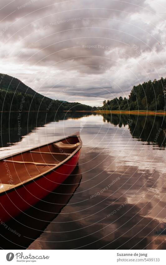 Wooden canoe on a river in sweden. The clouds are reflected in the river. The image has a picturesque, calm and peaceful vibe. The weather is cloudy, but the mood is happy.