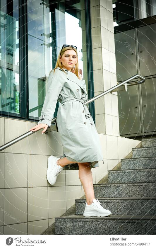 Portrait of a young woman in a trench coat and white sneakers on a staircase. Woman portrait Feminine feminine Looking Sunglasses Trench coat Stairs stagger