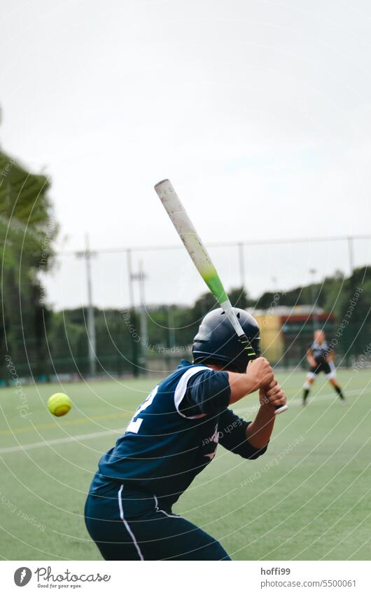 Softball player with back to camera has an approaching ball firmly fixed and takes a swing to hit it Baseball Lawn lawn sports Sports Ball Grass Playing