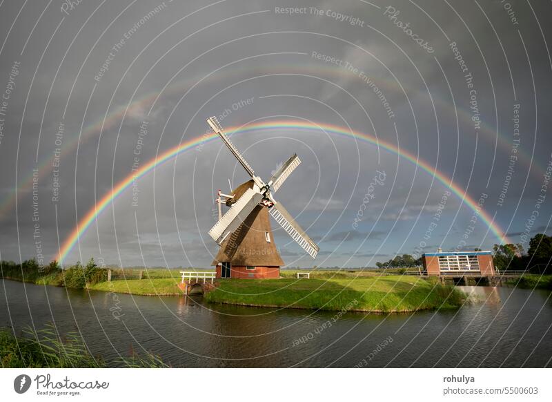 big double rainbow over Dutch windmill raining rainy river canal water lake horizon sunny wind turbine sky cloud cloudscape colorful multicolor purple orange