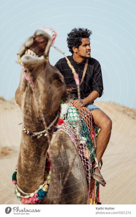 a young man sitting on a camel making a funny face Funny Man portrait One animal Camel Desert out India Sahara animals Vacation & Travel Tourism Colour photo