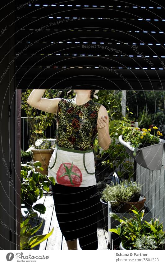 Woman standing on the balcony drinking something, her face is covered by the shutter of the balcony door Terrace green plants Garden Potted plants Gardening