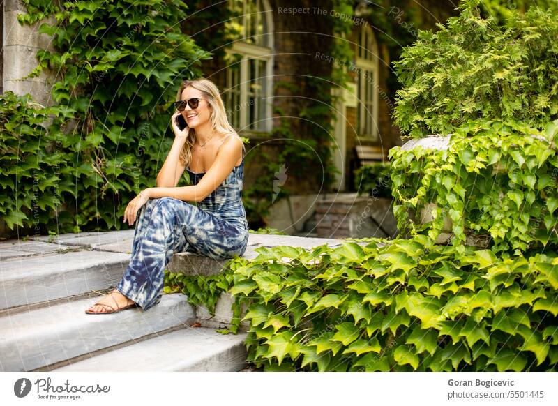 Pretty young woman using mobile phone by the old house with ivy sunglasses sitting cute caucasian adult attractive beautiful call cellphone communication