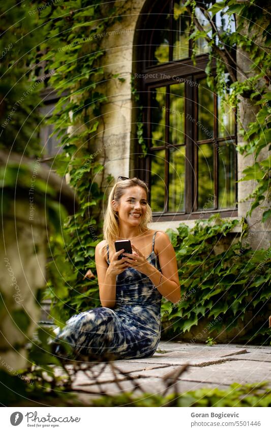 Pretty young woman using mobile phone by the old house with ivy sunglasses sitting cute caucasian adult attractive beautiful call cellphone communication