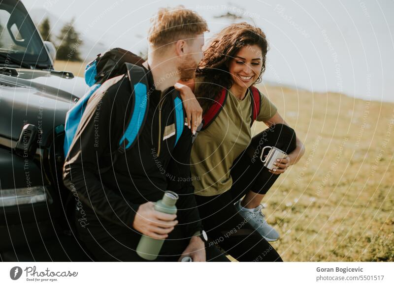 Young couple relaxing by a terrain vehicle hood at countryside adult adventure attractive auto automobile break calm car caucasian day drink drinking enjoy
