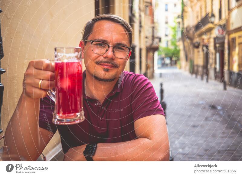 young man with glasses and short hair sits at a table holding a glass of Tinto de Verano Granada Red wine Spain Andalucia Bar Tapas bar Refreshment Cold drink